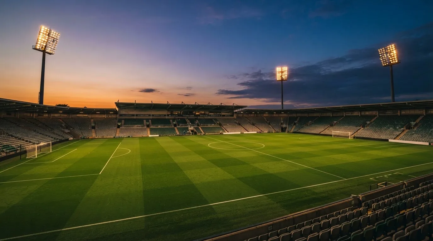 An empty football stadium with floodlight masts at dusk