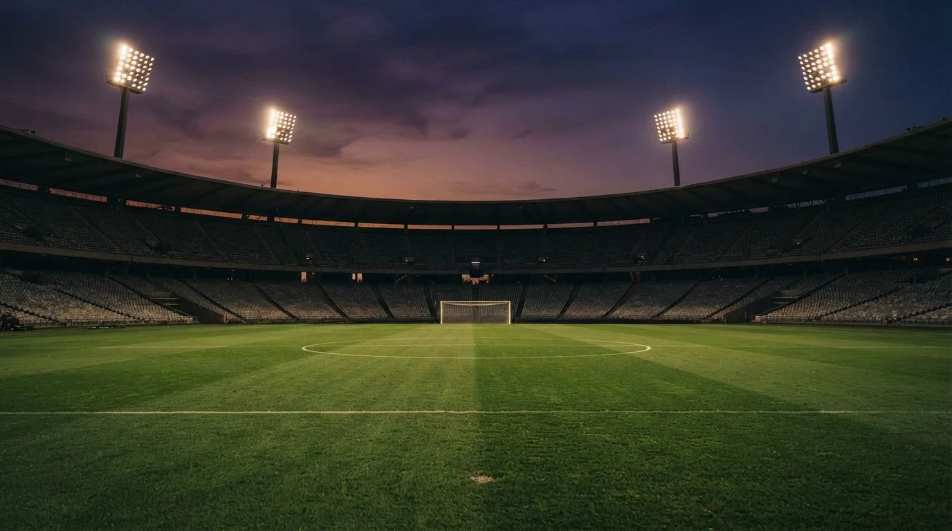 An empty football stadium with floodlight masts at dusk